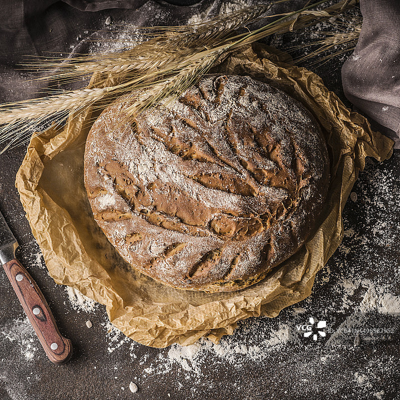 深色乡村背景下的自制新鲜酸面包，配有面粉和麦穗图片素材