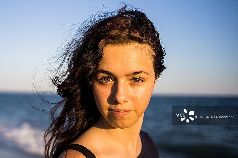 年轻漂亮的黑发女孩在日落时分的海边沙滩上微笑图片素材