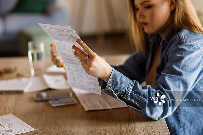 年轻女子在整理家庭财务时阅读财务账单上的数值图片素材