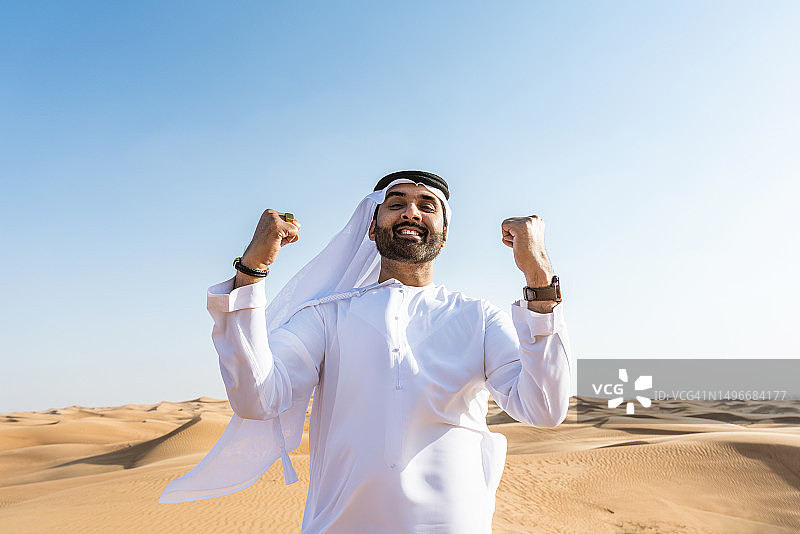 男子在沙漠中举起双臂，背景是晴朗的天空图片素材