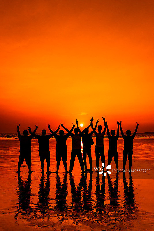 橙色天空下海滩上跳舞的人群剪影图片素材