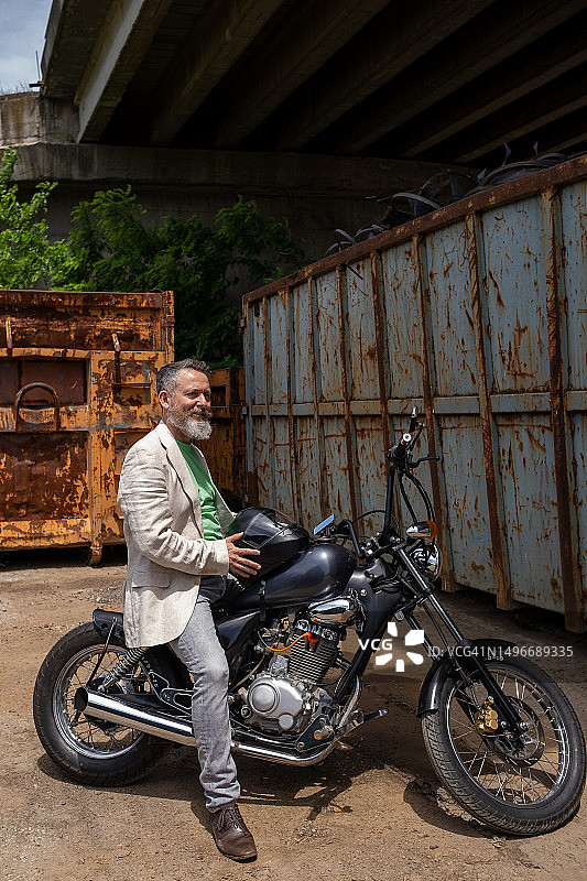一位中年男人穿着浅绿色T恤、米色夹克和灰色牛仔裤，骑着一辆Bobber摩托车图片素材