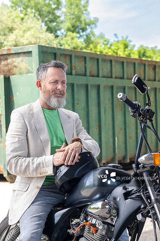 一位中年男人穿着浅绿色T恤、米色夹克和灰色牛仔裤，骑着一辆Bobber摩托车图片素材