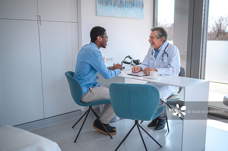 中年成年黑人男性病人和中年白人医生在医生办公室图片素材