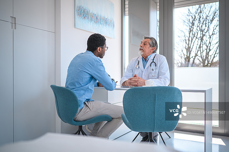 中年白种人皮肤科医生与一位中年黑人男子的医疗预约图片素材
