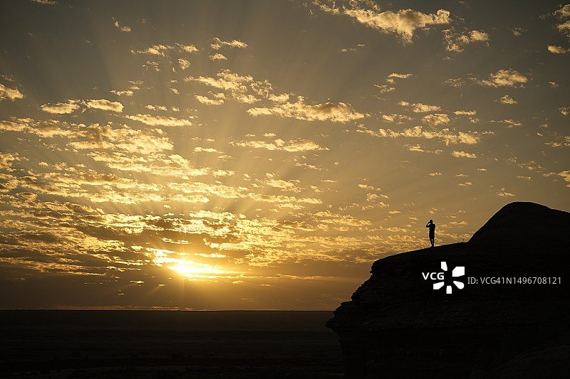日落时分，男子站在悬崖边，以天空为背景的轮廓图片素材