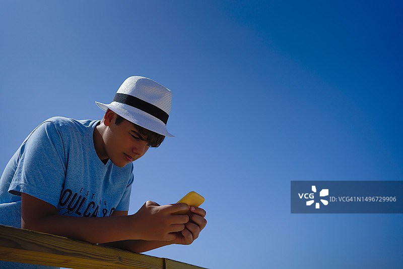戴白帽靠木栏杆看手机的少年图片素材
