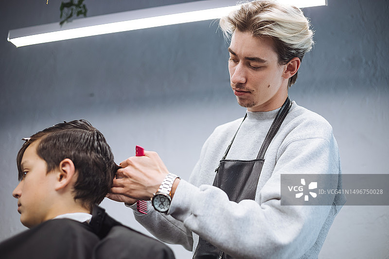 年轻发型师用专业工具为少年理发图片素材