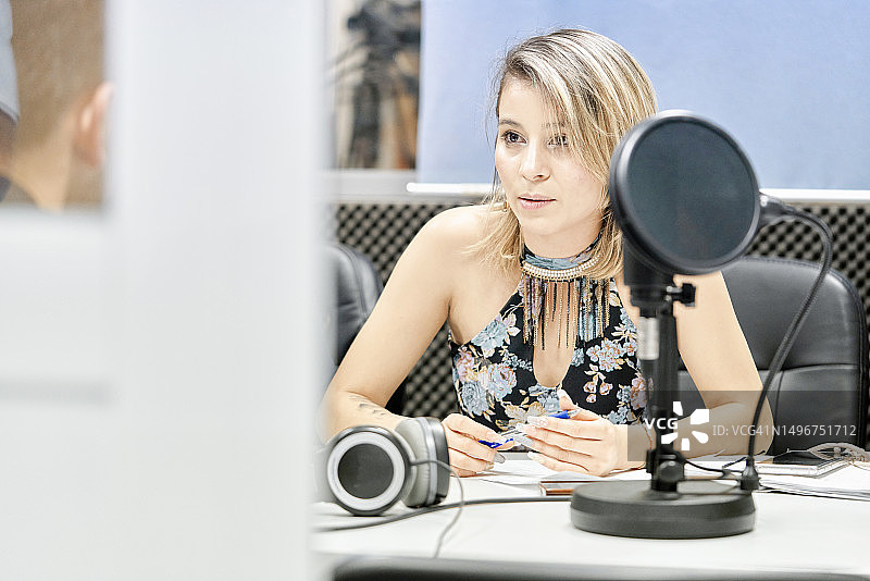 正面视角：美丽的女士坐在广播电台，对着麦克风与她的伙伴交谈图片素材