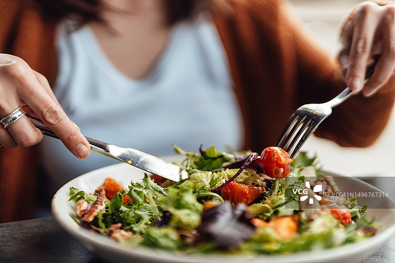 年轻女子在餐厅吃蔬菜沙拉的特写镜头图片素材
