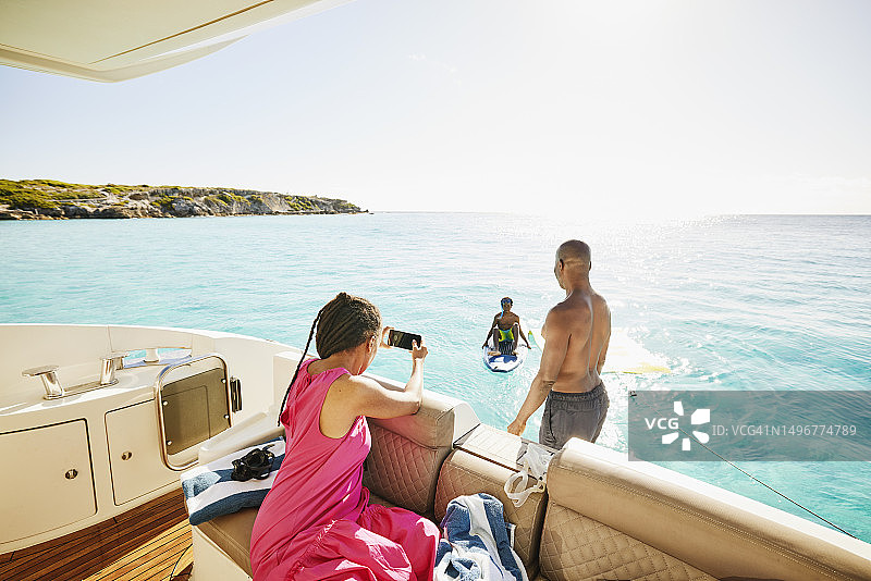 母亲为在海中玩桨板的儿子拍照的后视图图片素材