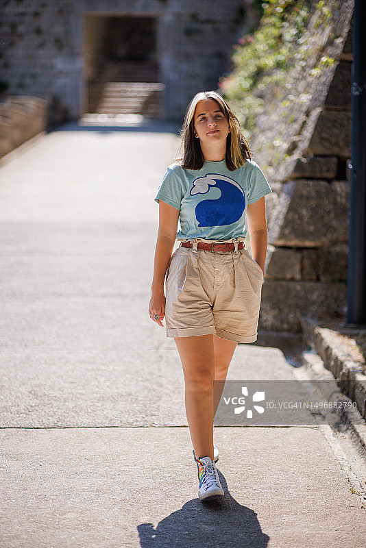 美丽的少女在阳光明媚的日子里，在古老的岛屿小镇的人行道上散步图片素材