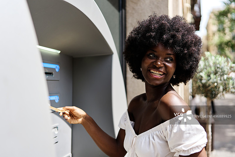 在自动取款机上使用银行卡取款的蓬松发型黑人女性图片素材