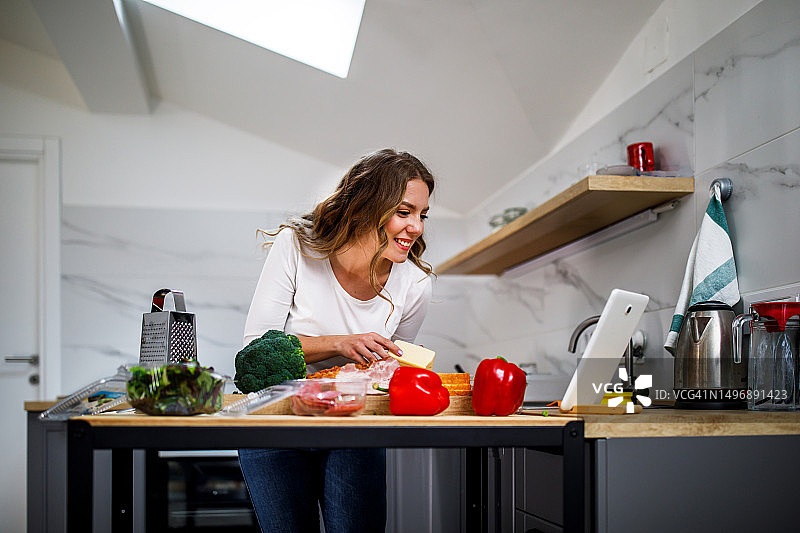 年轻女子正在使用平板电脑的在线帮助准备晚餐图片素材