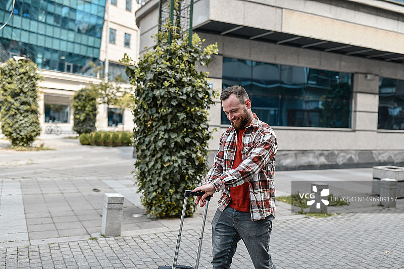 快乐的络腮胡男人在新城市里拉着旅行包图片素材