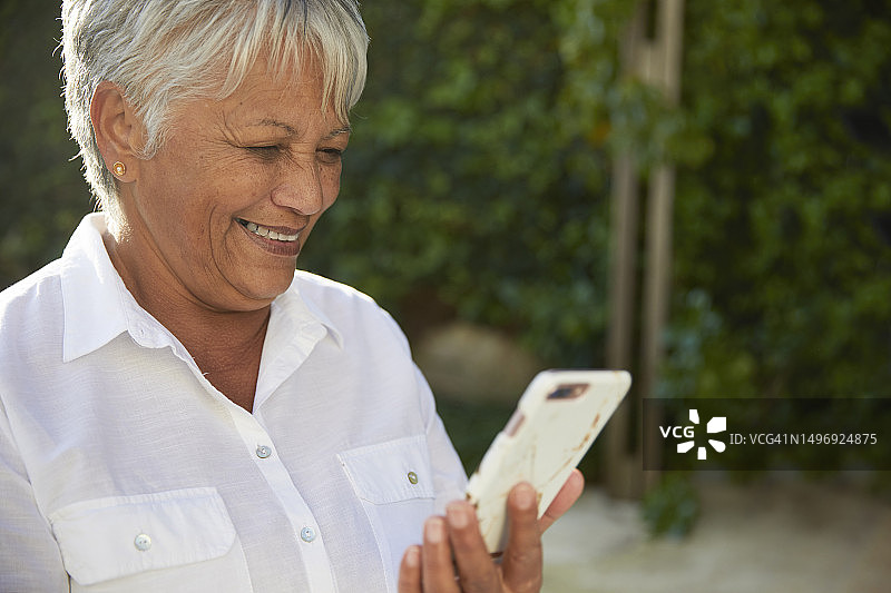 漂亮的老年女性看着她的手机笑图片素材