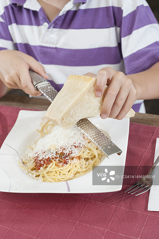 男孩在意大利面上磨碎奶酪，德国巴伐利亚州图片素材