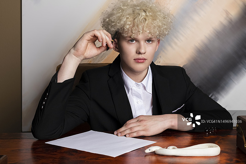 时尚金发男子与白化球蟒，纯白蛇在商人木桌上爬行图片素材