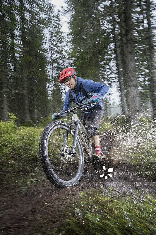 山地自行车手在雨天穿越萨尔费尔登蒂罗尔奥地利森林中的水坑图片素材