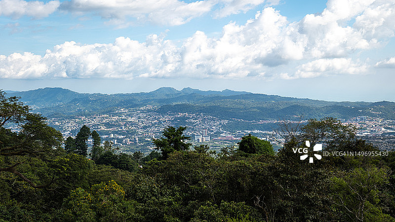 从远处在白天的多云天空下看到的森林上方的城市景观全景图片素材