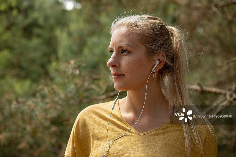 戴着耳机和马尾辫的金发女子站在森林背景前图片素材