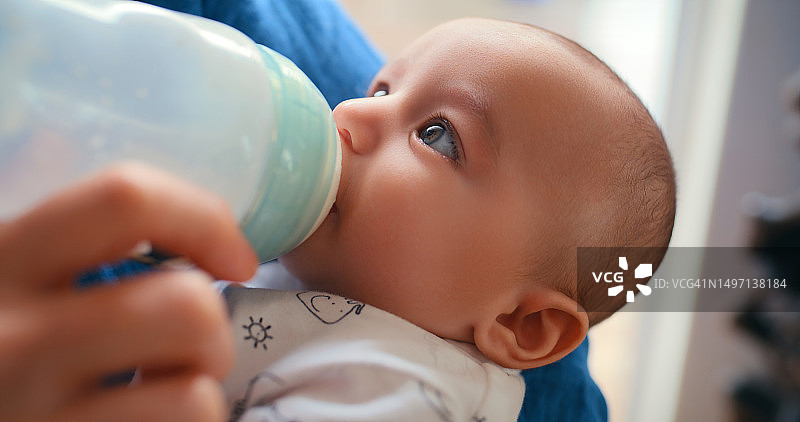 宝宝的脸、奶瓶和喂养孩子的人的手，为新生儿或婴儿提供成长、健康的身体和家庭支持。营养、配方奶或幼儿饮用液体，以呵护骨骼、保持健康图片素材