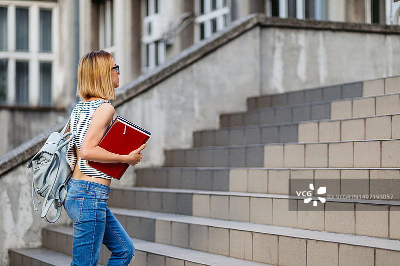 手捧书本爬楼梯的女大学生图片素材