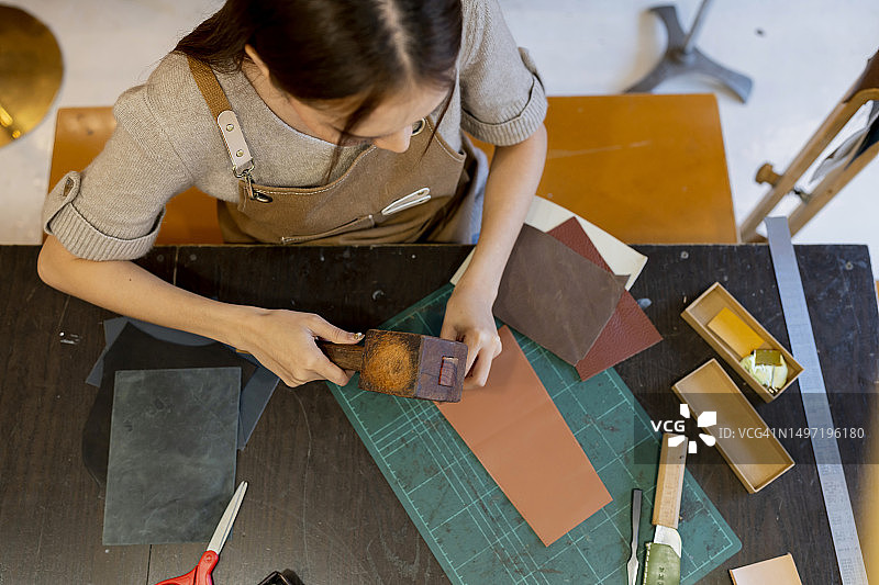 年轻女性皮革匠使用木槌和冲孔工具制作皮带特写图片素材