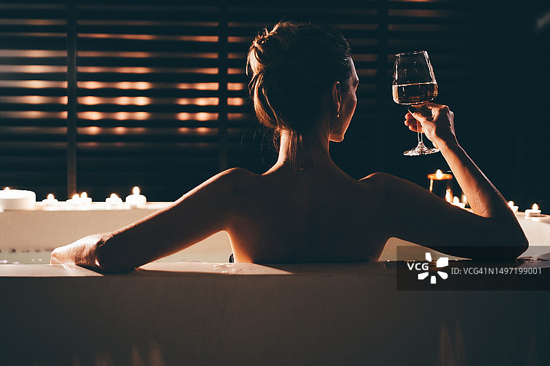 美丽的女人在夜晚的烛光浴缸里放松并品尝葡萄酒图片素材