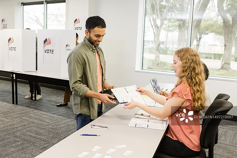 年轻男子在投票站从女性志愿者手中接过选票图片素材