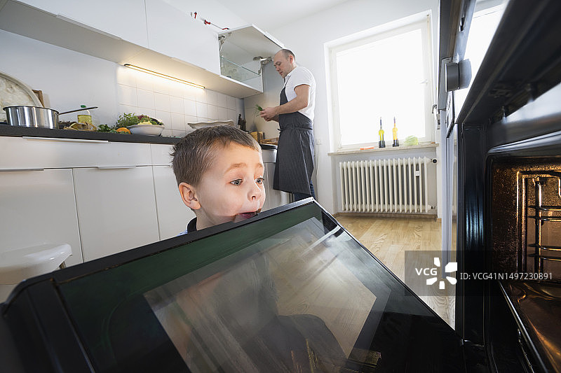 父亲做饭，饥饿的儿子看着烤箱图片素材