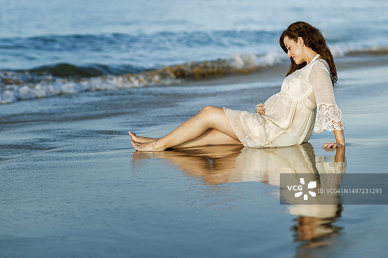 海滩上身穿白色连衣裙的孕妇图片素材