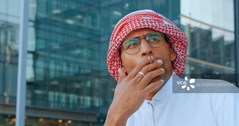 在城市户外吸烟休息的穆斯林商务男士，伊斯兰教、烟瘾和尼古丁烟雾图片素材