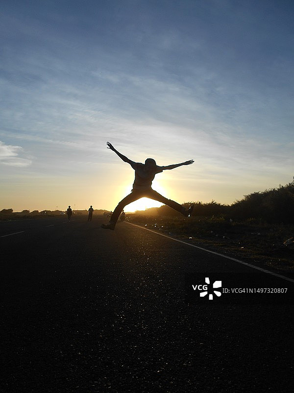 一个男人在日落背景下跳跃图片素材