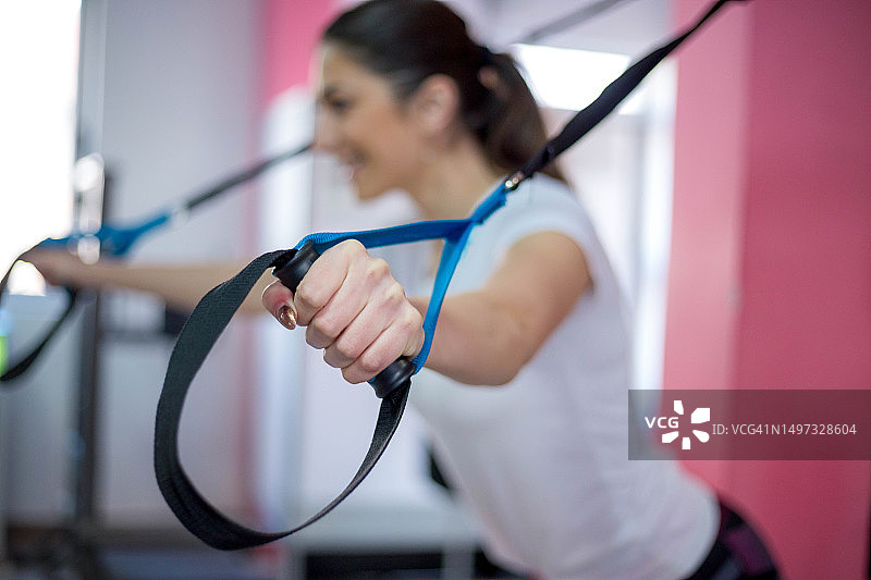 年轻的健身女人在健身房使用悬挂训练系统做运动。运动、健身、训练、人物概念图片素材