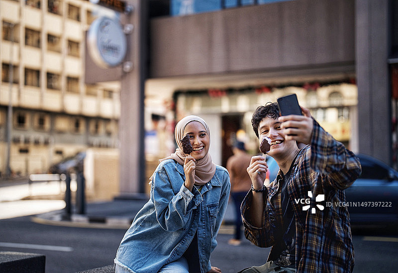亚洲年轻人街头用智能手机吃冰淇淋并在社交媒体上分享图片素材