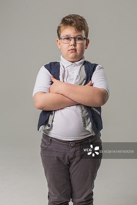 戴眼镜的金发男孩穿着牛仔裤和背心在灰色背景的工作室里图片素材