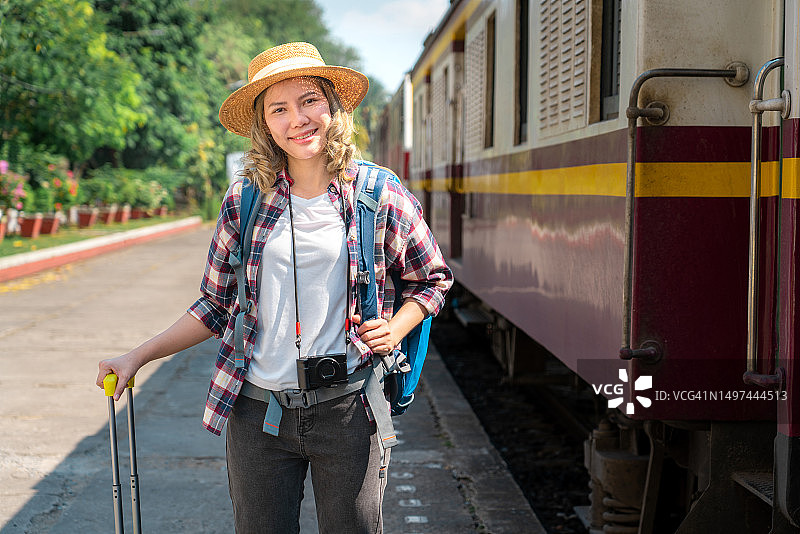 在火车站行走的女游客。年轻的亚洲女游客背着背包，拖着行李在铁路上。积极的旅行生活方式概念图片素材