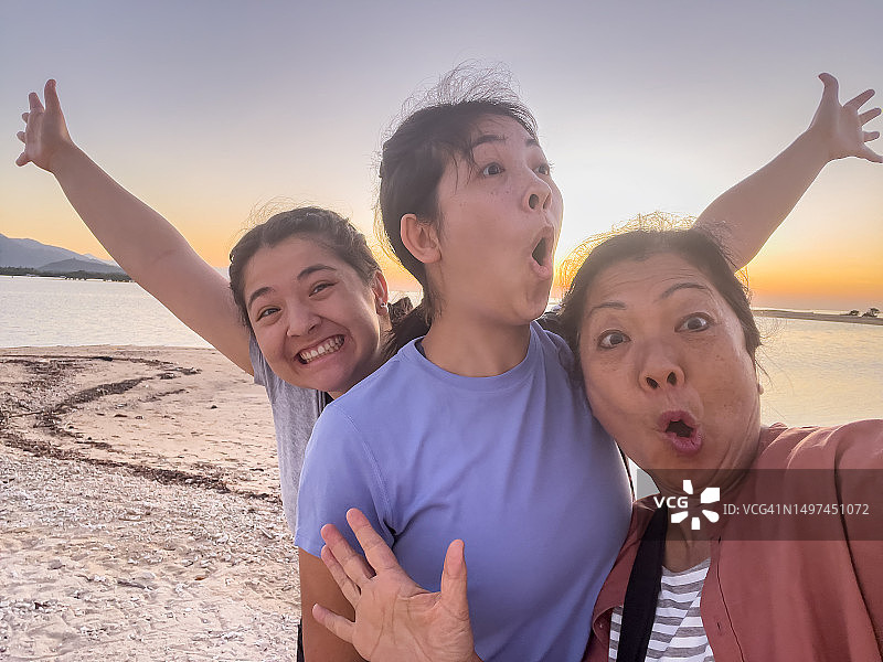 在海滩上用手机搞怪自拍的亚裔母亲和混血女儿们图片素材