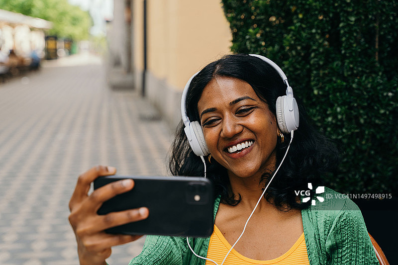 坐在路边咖啡馆，用耳机通过视频会议通话的千禧一代印度女人图片素材