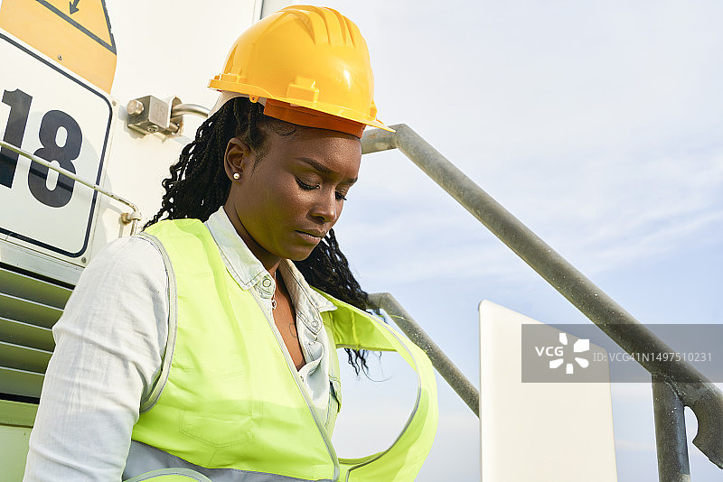 长发棕发女人戴着头盔坐在户外楼梯上专注于电脑，低角度图片素材