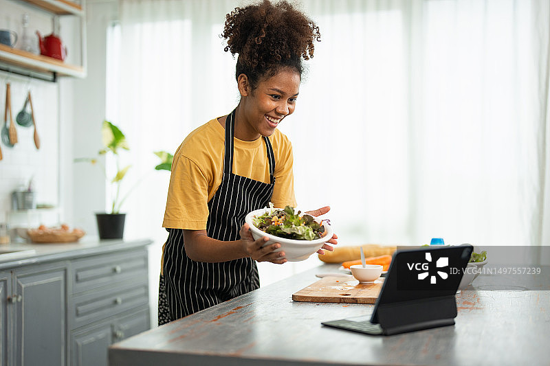 女子在厨房烹饪生菜并与朋友视频聊天图片素材