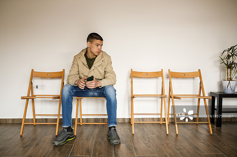 坐在候诊室椅子上等待的青少年男孩图片素材