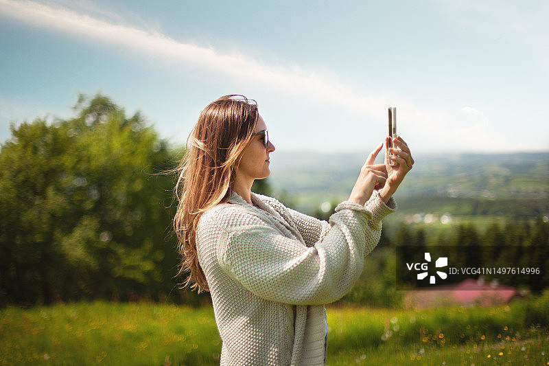 在山区绿色草地上使用智能手机的美丽女人图片素材