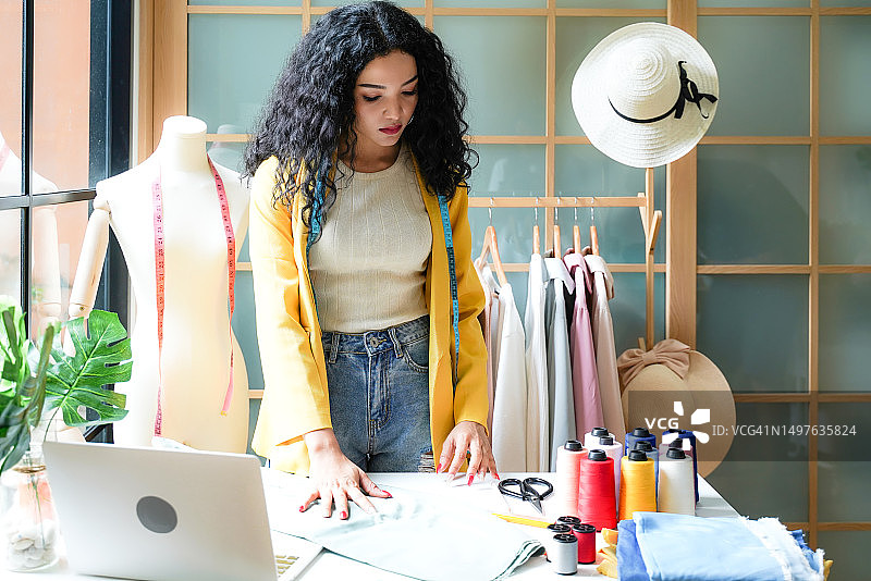 年轻女服装设计师在展厅使用笔记本电脑工作并接收客户的设计订单图片素材
