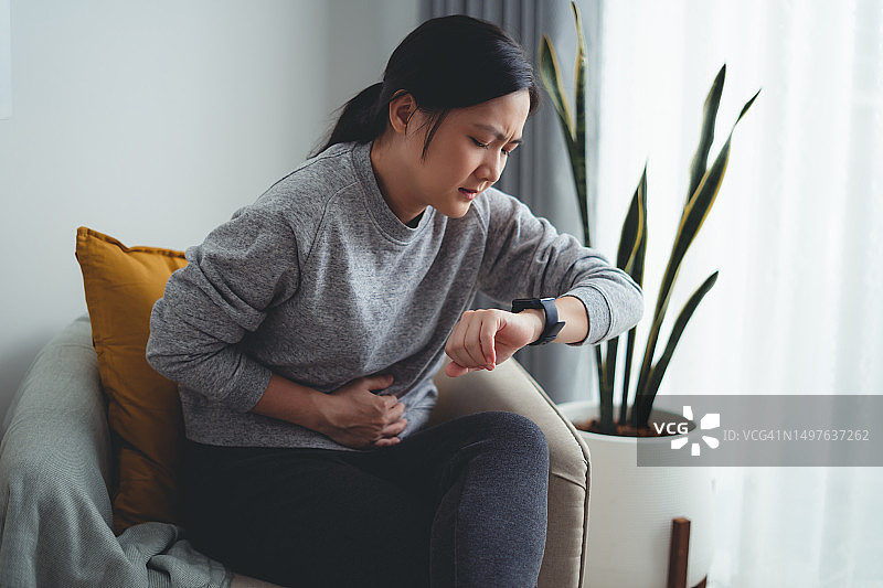 亚洲女人在家中客厅的扶手椅上感到胃痛图片素材