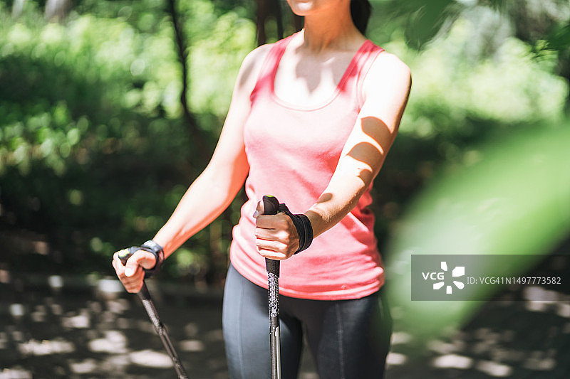 身穿运动服的年轻黑发女子在夏日公园里用手杖进行北欧式健走图片素材