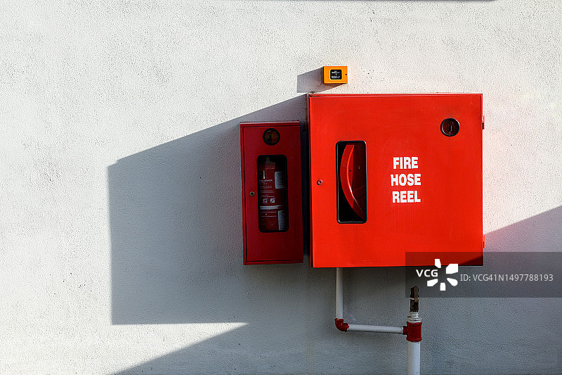 白色墙壁上的灭火器和消防软管卷盘图片素材