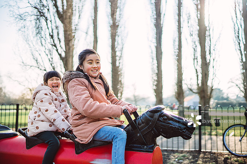 快乐的姐妹在操场上骑摇马图片素材