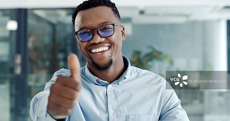 快乐自信的年轻商人竖起大拇指，在现代化的办公室里表示赞同。男性商务人士面带微笑，看起来很高兴图片素材